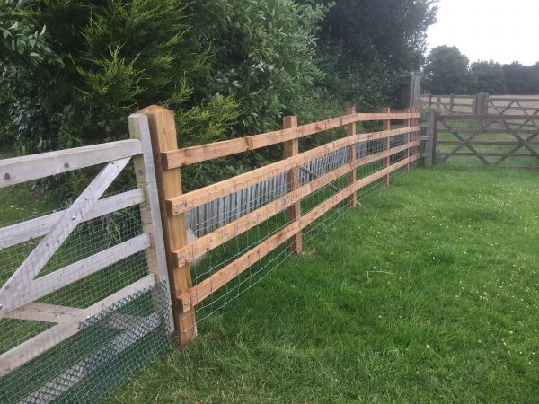 Commercial fence and gate surrounding a field. The fence is of a post and rail style perfect for a rural look.