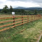 Post and rail fencing standing in a empty field. Commercial fencing perfect for securing livestock.