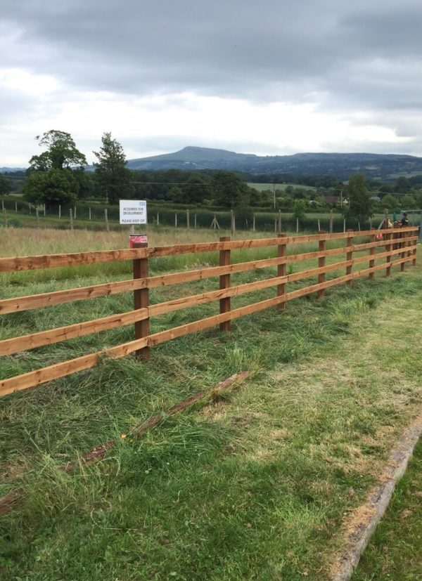 Post and rail fencing standing in a empty field. Commercial fencing perfect for securing livestock.