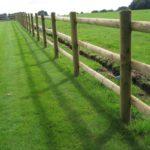 Round wooden fence posts and rails on a green field. Perfect for commercial fencing needs.