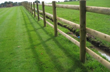 Round wooden fence posts and rails on a green field. Perfect for commercial fencing needs.