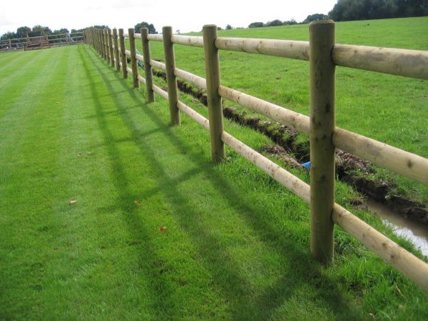 Round wooden fence posts and rails on a green field. Perfect for commercial fencing needs.