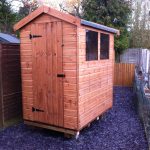 Made to measure garden shed stood in a garden with a gravel ground. The bespoke shed has two glass windows and a door.