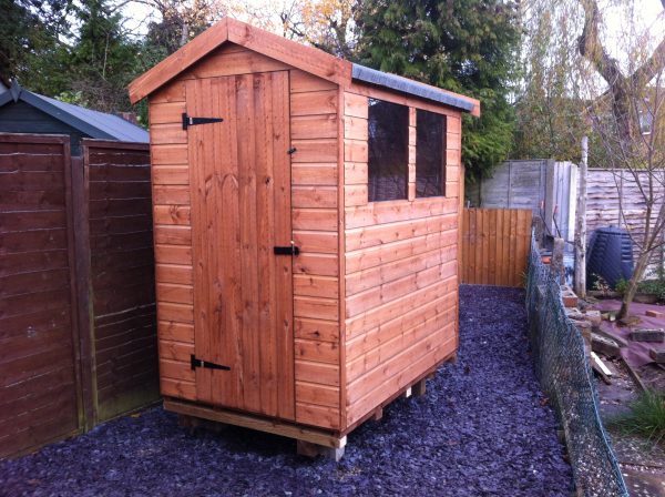 Made to measure garden shed stood in a garden with a gravel ground. The bespoke shed has two glass windows and a door.