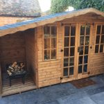Made to measure garden shed standing in a yard beside a wall of ivory. This bespoke shed has glass windows and doors.
