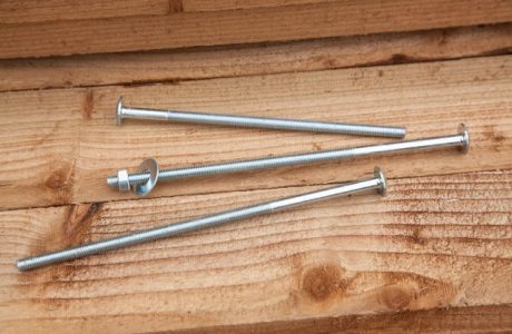 Three steel roofing bolts fitting on a wooden fence panel