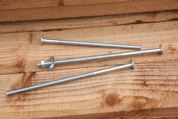 Three steel roofing bolts fitting on a wooden fence panel