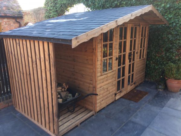 Made to measure garden shed in a garden. This bespoke shed has a slate roof and a log store on the side.