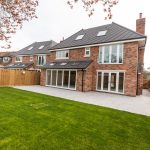 A house and garden with green grass and feather edged wooden fencing.