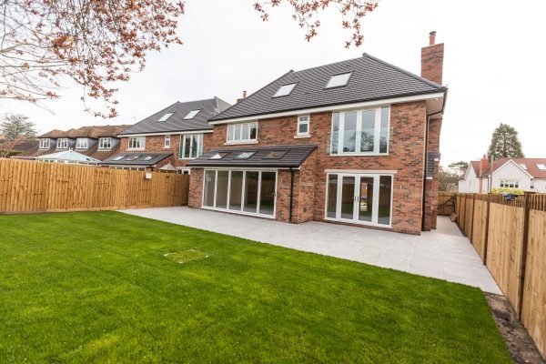 A house and garden with green grass and feather edged wooden fencing.