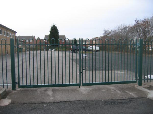 Green steel palisade gates stand in front of an empty yard. These commercial gates are perfect for securing school yards.