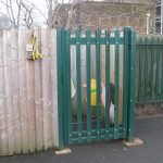 Green palisade gates attached to a wooden fence surrounding a school yard. Commercial gates and fencing great for security.