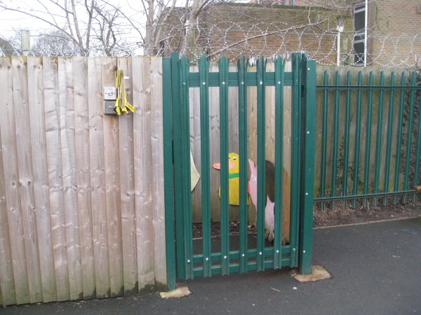 Green palisade gates attached to a wooden fence surrounding a school yard. Commercial gates and fencing great for security.