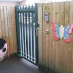 A green steel palisade gate securing a school yard.