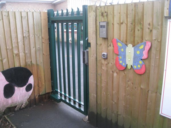 A green steel palisade gate securing a school yard.