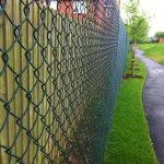 Green chain linking fence alongside a public walkway. Commercial fencing provides security for many different areas.