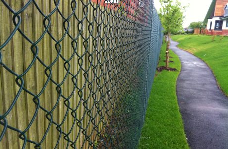 Green chain linking fence alongside a public walkway. Commercial fencing provides security for many different areas.