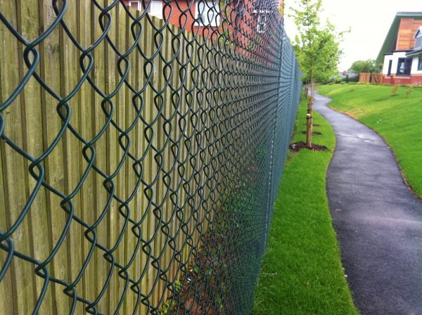 Green chain linking fence alongside a public walkway. Commercial fencing provides security for many different areas.