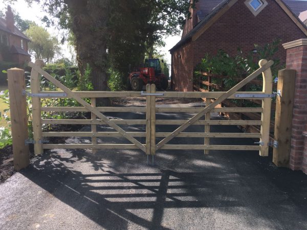 A closed five bar field gate. Two wooden posts stand at either side. The gate is used for commercial purposes on a farm.