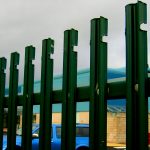 Green steel palisade fencing surrounding a commercial building.