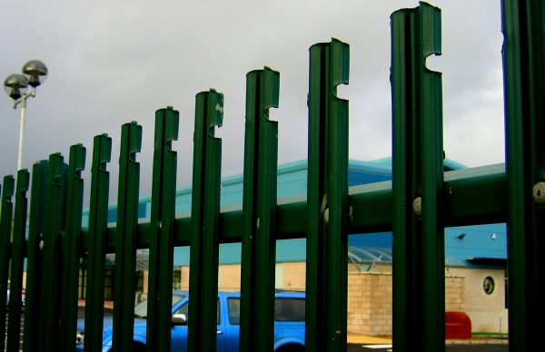 Green steel palisade fencing surrounding a commercial building.