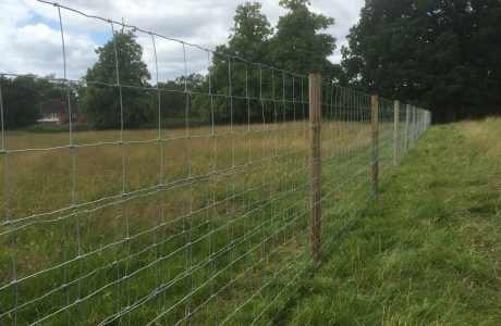 A long fence with round fence posts. The fence stands on a empty field.