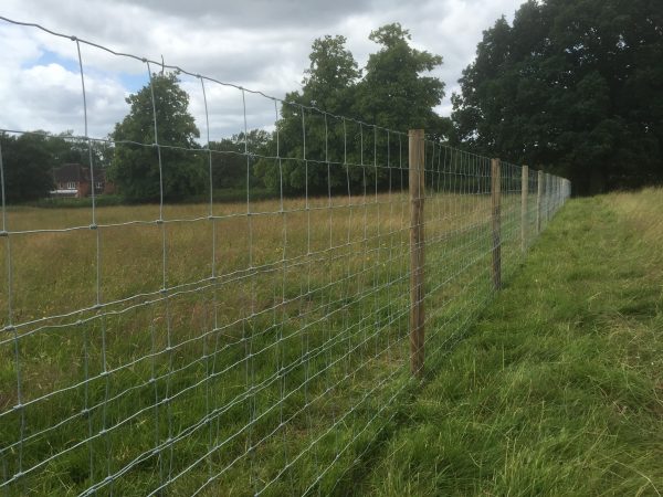 A long fence with round fence posts. The fence stands on a empty field.