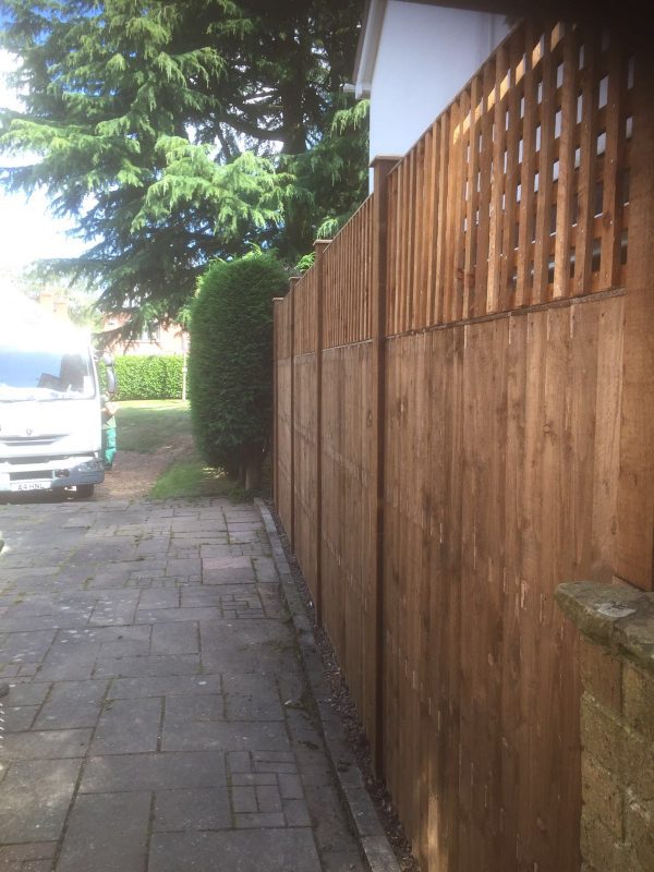 A wooden fence next to a large vehicle. It is a v type fence with close board fence panels.