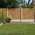 A garden with plants and flowers with a fence surrounding the perimeter. The fence has close board fence panels.