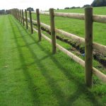 A open field with a commercial fence. The fence has round fence posts and half round fence posts.