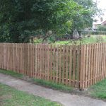 A wooden fence surrounding a large garden or allotment. The ween fence is made up many timber pales.