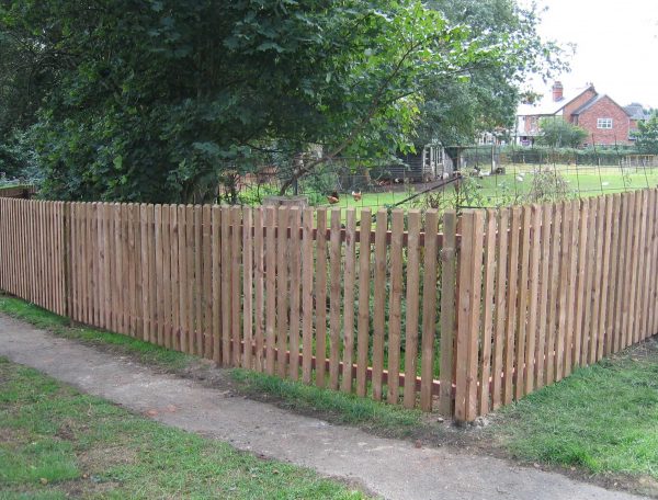 A wooden fence surrounding a large garden or allotment. The ween fence is made up many timber pales.