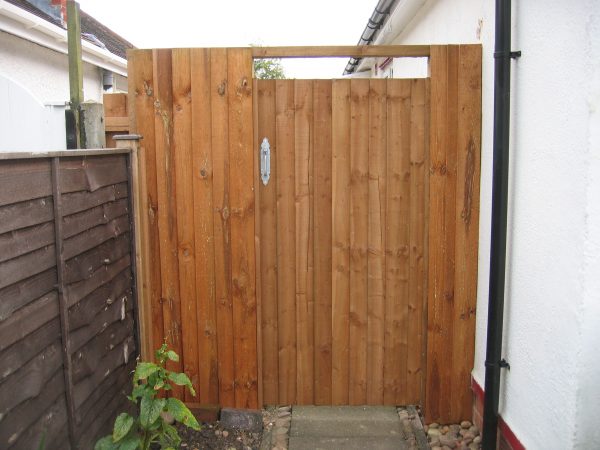 A wooden gates stands at the side of a house. The gate has feather edge boards with a pre-clad timber frame.
