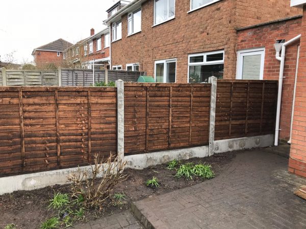 A house with a wooden fence alongside. The fence has z type timber panels which are double framed, overlapped with bevelled capping.