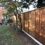 A house with a wooden fence running around the outside. The fence is supported with concrete fence posts.