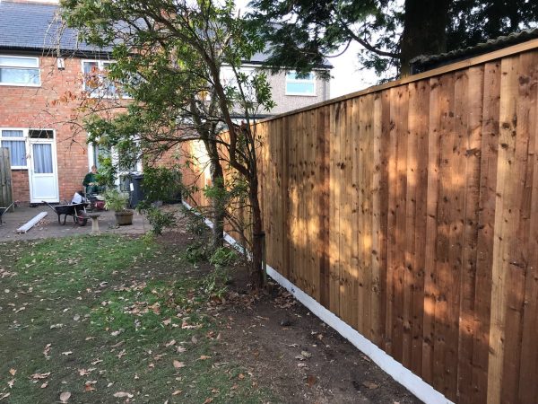 A house with a wooden fence running around the outside. The fence is supported with concrete fence posts.