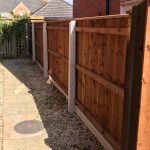 Concrete fence posts support four wooden fence panels on a empty garden.