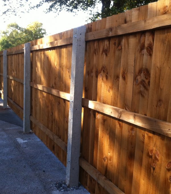 Concrete fence posts supporting wooden fence panels. The fence is on display in a supply yard in Birmingham.