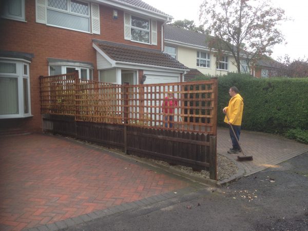 Two people stand behind a wooden fence. The fence has t type timber trellis fencing panels.