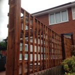 A fence divides two houses. The fence has t type timber trellis fencing panels.