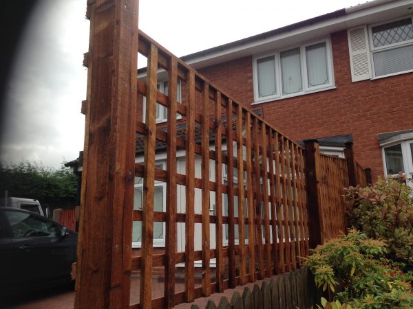 A fence divides two houses. The fence has t type timber trellis fencing panels.