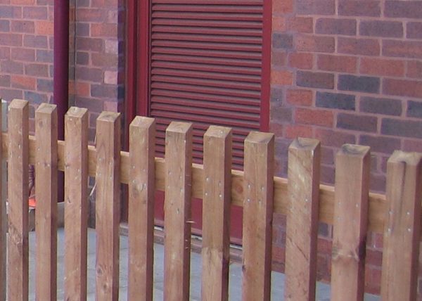 A wooden fence standing in front of a commercial building. The fence is constructed using timber pales.