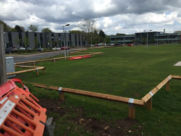 Bird mouth posts surround a large park like area. Commercial buildings and businesses stand at either side.