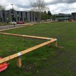 Bird mouth posts surround a large open space. Commercial buildings stand at either side.