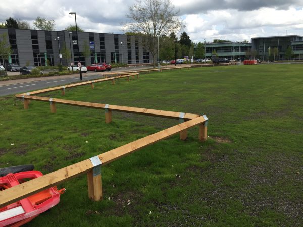 Bird mouth posts surround a large open space. Commercial buildings stand at either side.