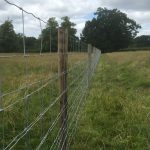 A long post and wire fence is used on a empty field to divide the open space.
