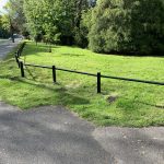 A open space with a steel trip rail separating a grass space from a public path.